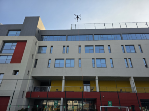 DRONICLE cleaning drone washing a painted school wall and windows in Dubai using professional drone-powered exterior cleaning technology
