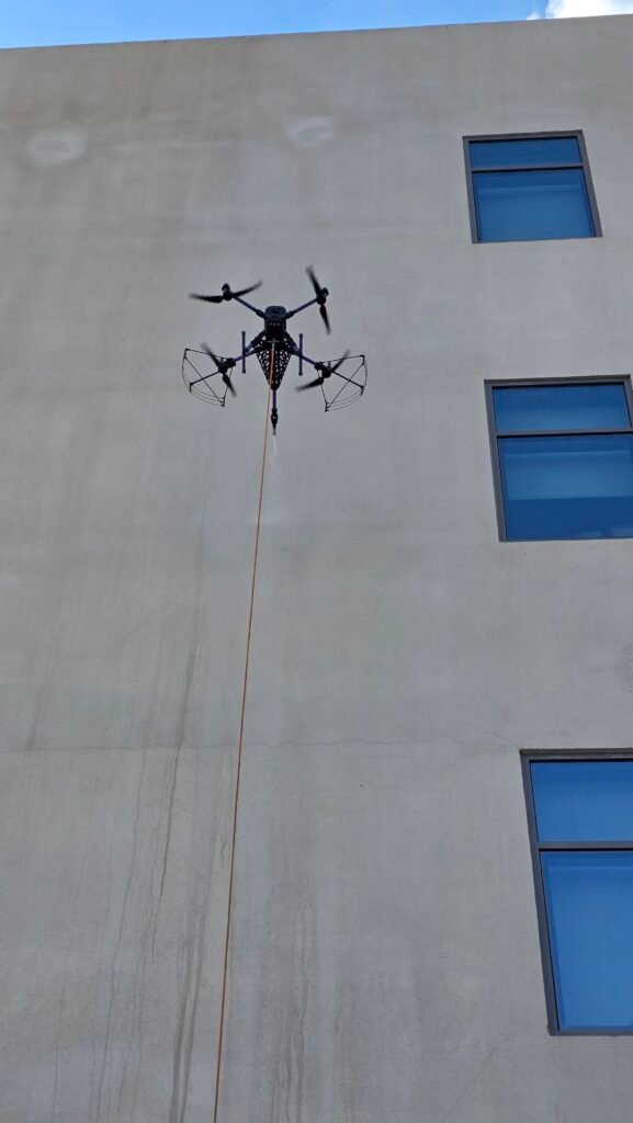 School facade cleaning in Dubai using DRONICLE drone and techonolgy. The dust is flowing down while spraying fresh water.